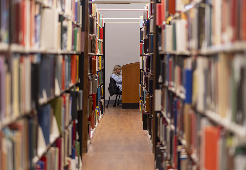 A student can be seen studying past the rows of books in the library