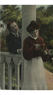 1909 Postcard showing a couple on a porch, a woman picking flowers and a man behind her.